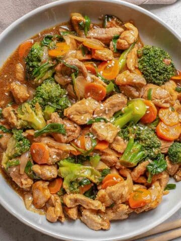 Pork chop suey prepared on a white plate with chopsticks on the side on a white background.