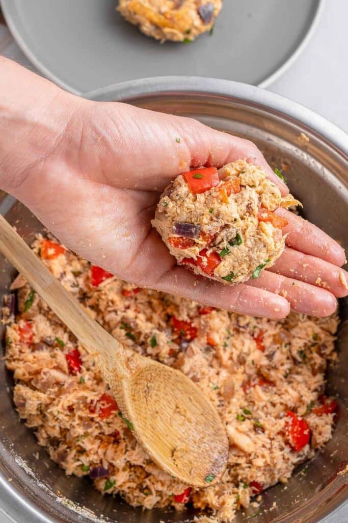 A person's hand holding a salmon croquette patty.
