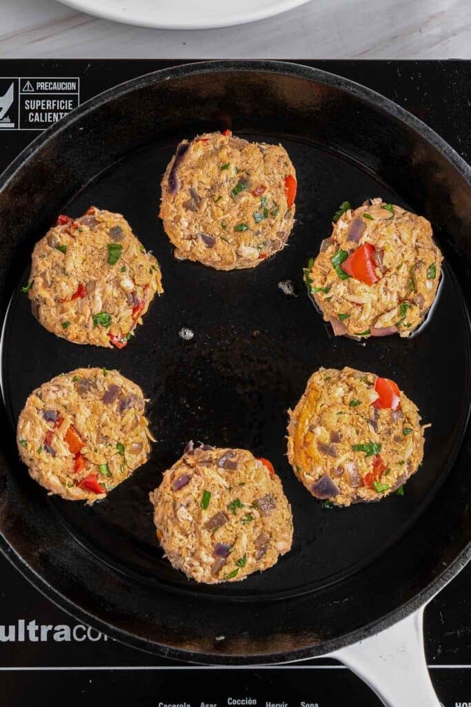 Six patties of the salmon croquette being cooked in a large skillet.