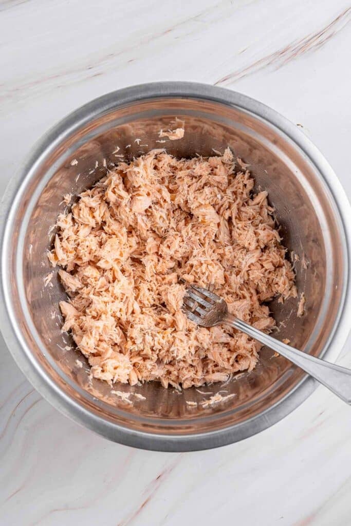 Shredded cooked salmon in a large stainless bowl.
