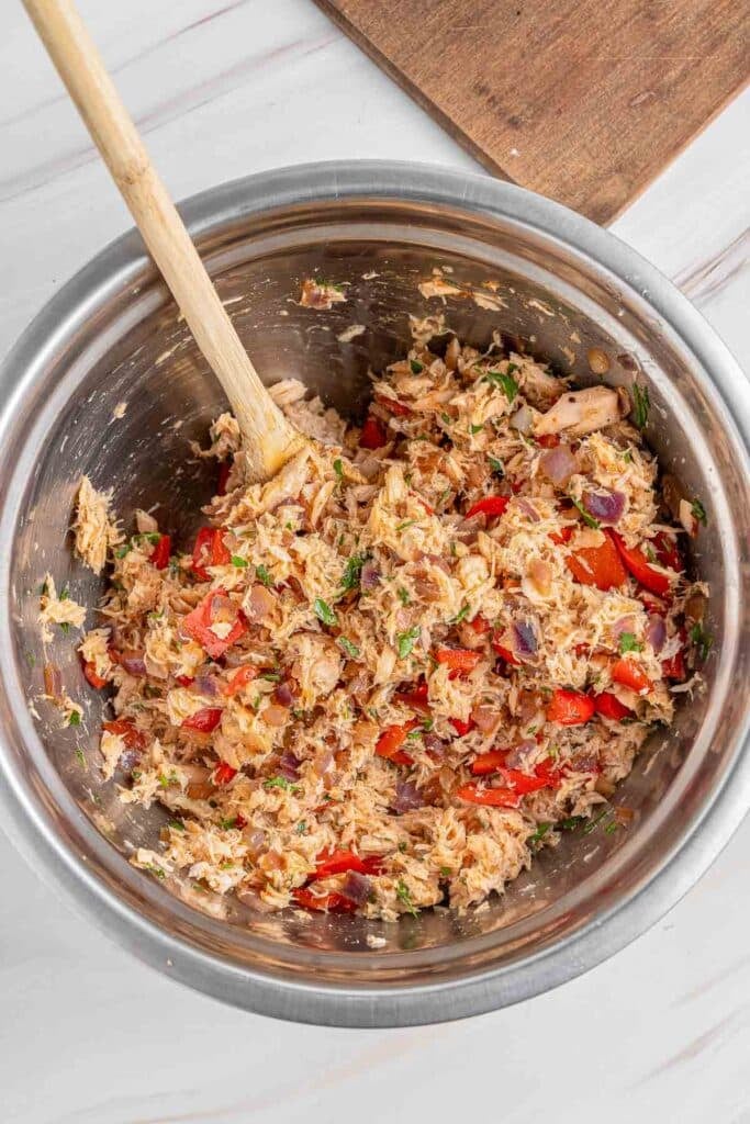 A large mixing bowl containing ingredients for salmon croquettes with a wooden spoon inside the bowl ready to mix.