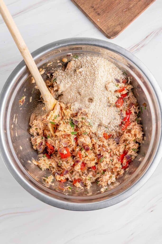 A large mixing bowl containing ingredients for salmon croquettes with a wooden spoon inside the bowl ready to mix.