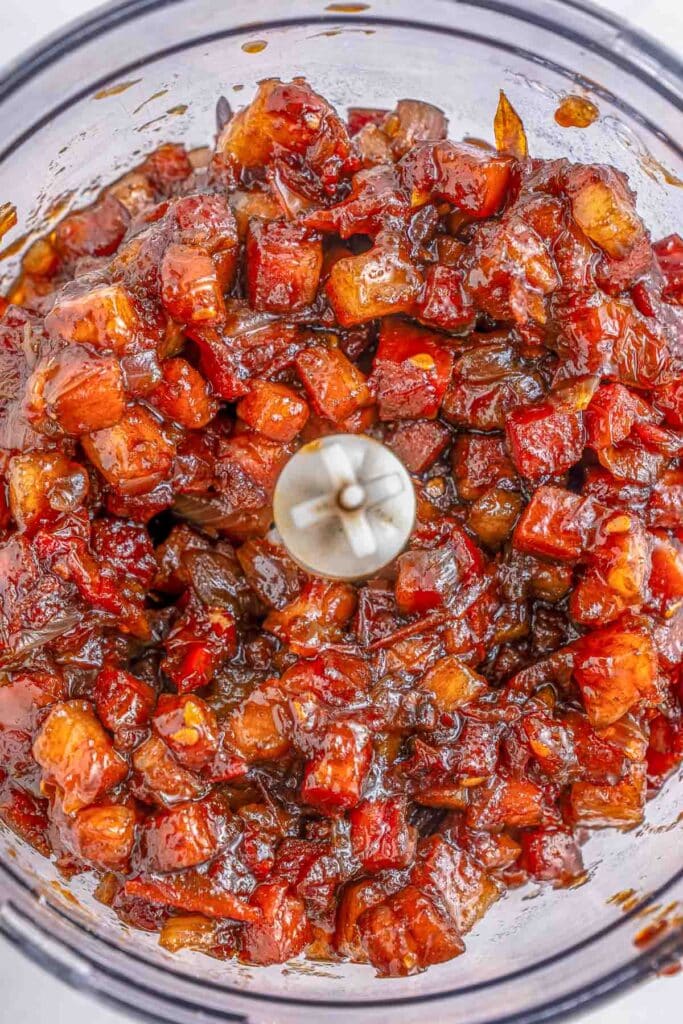 A food processor bowl filled with a ingredients for tomato jam ready to be chopped together.