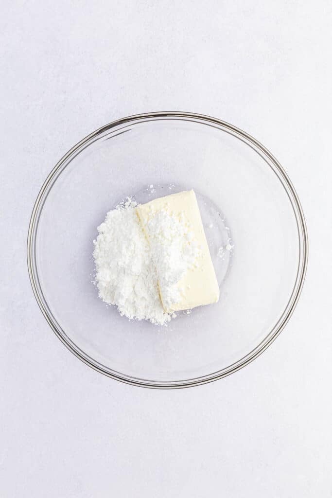 A clear glass bowl containing a a stick of cream cheese and powdered sugar.