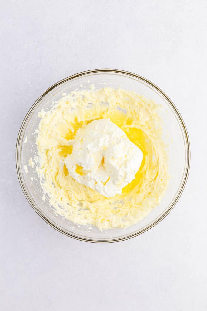 A clear glass bowl containing Cool Whip, lemon juice, and lemon extract mixed together.