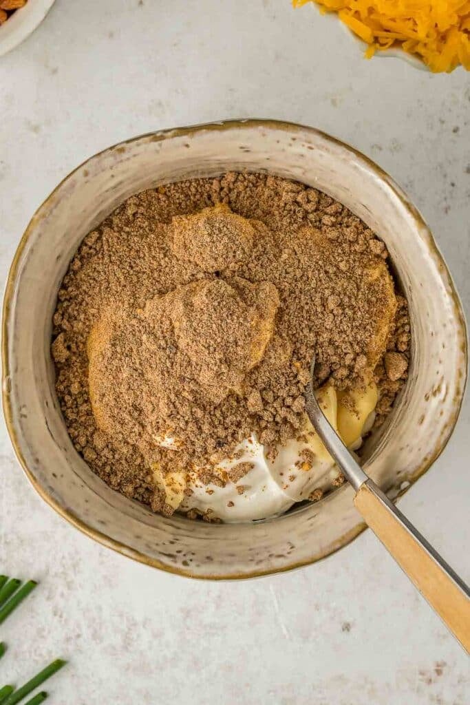 A mixing bowl containing mayonnaise, sour cream and ranch dressing mix with a spoon placed inside.
