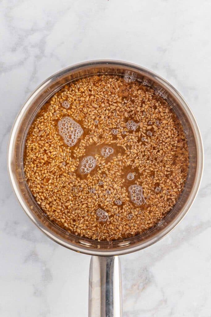 A saucepan filled with cooked bulgur wheat on a marble surface.