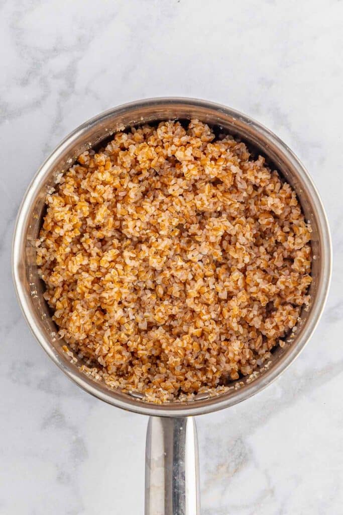 A metal pot with cooked bulgur wheat sits on a light-colored countertop.