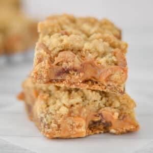 Two stacked carmelita bars with a visible layer of caramel and crumbled topping, placed on a white surface.