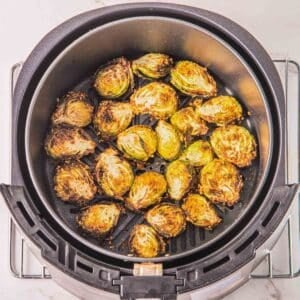 An air fryer on a metal rack containing slightly charred Brussels sprouts.