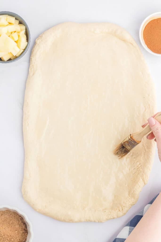The rolled out dough is being brushed with melted butter.