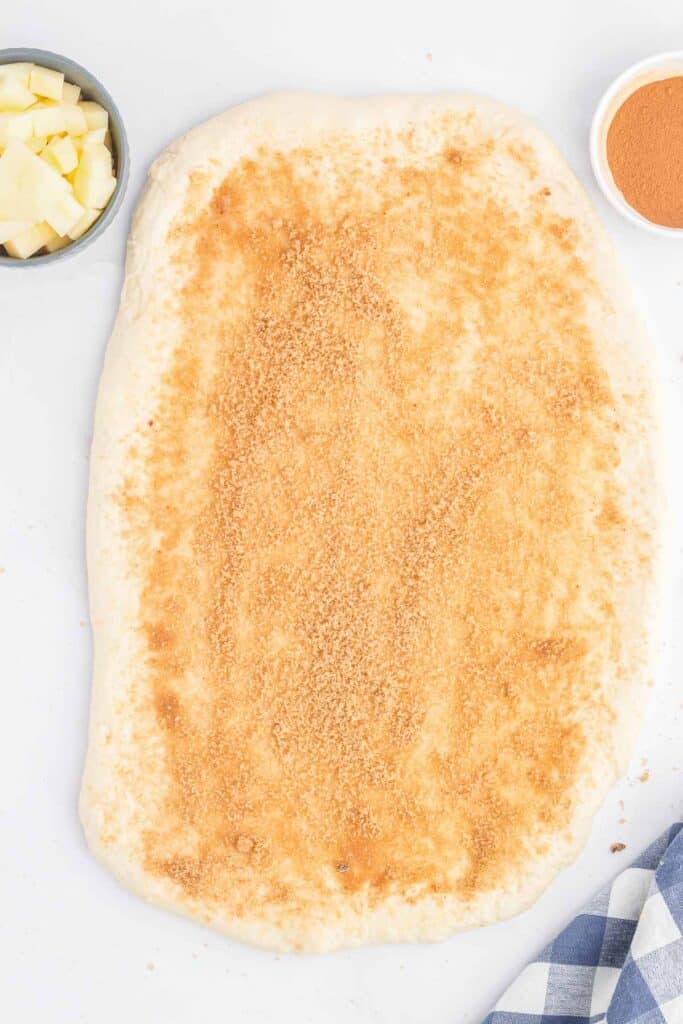 Dough rolled out on a surface, coated with a layer of brown sugar.