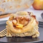 A single piece of apple cinnamon roll on a black plate with a fork.