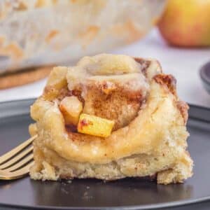A single piece of apple cinnamon roll on a black plate with a fork.