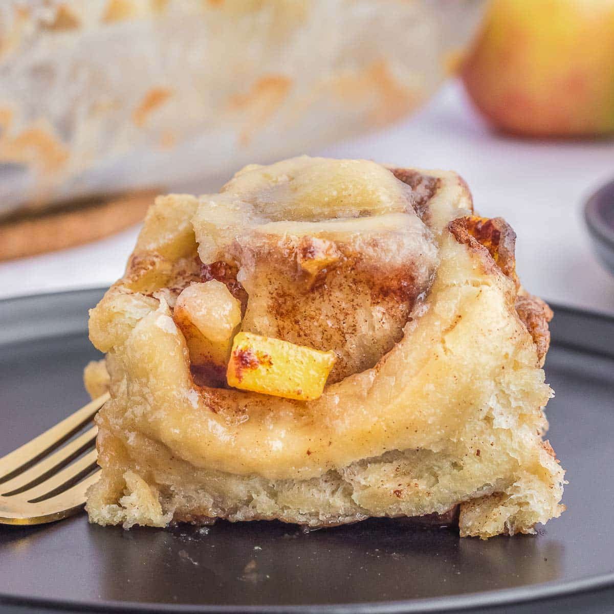 A single piece of apple cinnamon roll on a black plate with a fork.