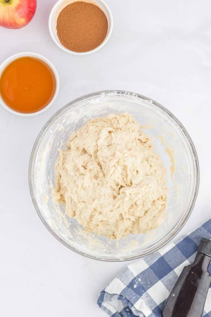 A large glass bowl with dough sits on a white surface.