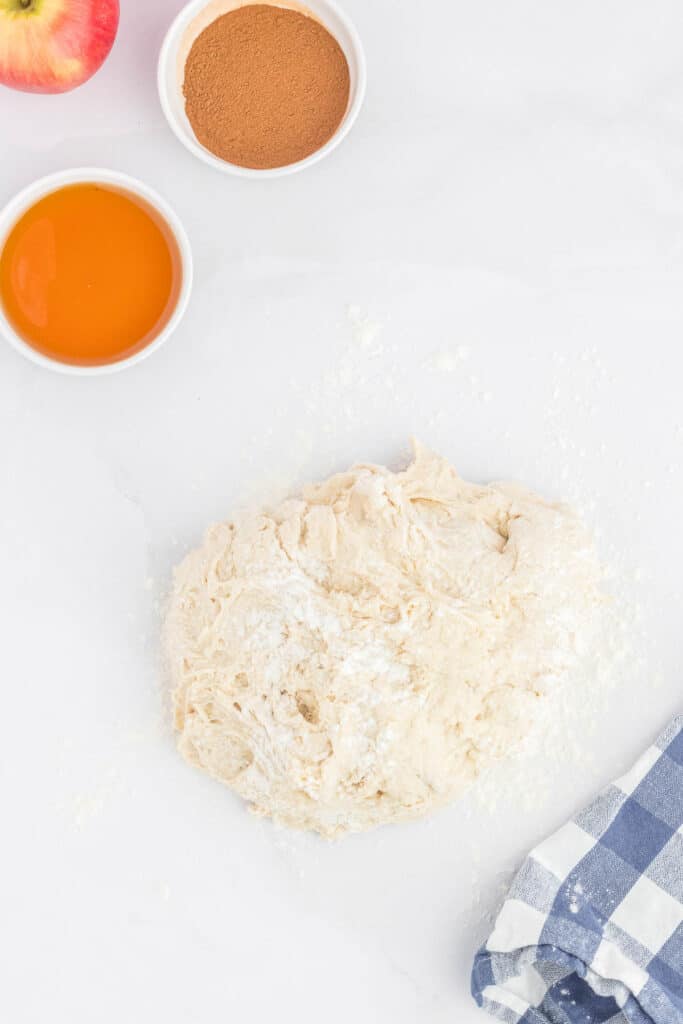 Dough on a floured countertop next to bowls of maple syrup and and cinnamon.