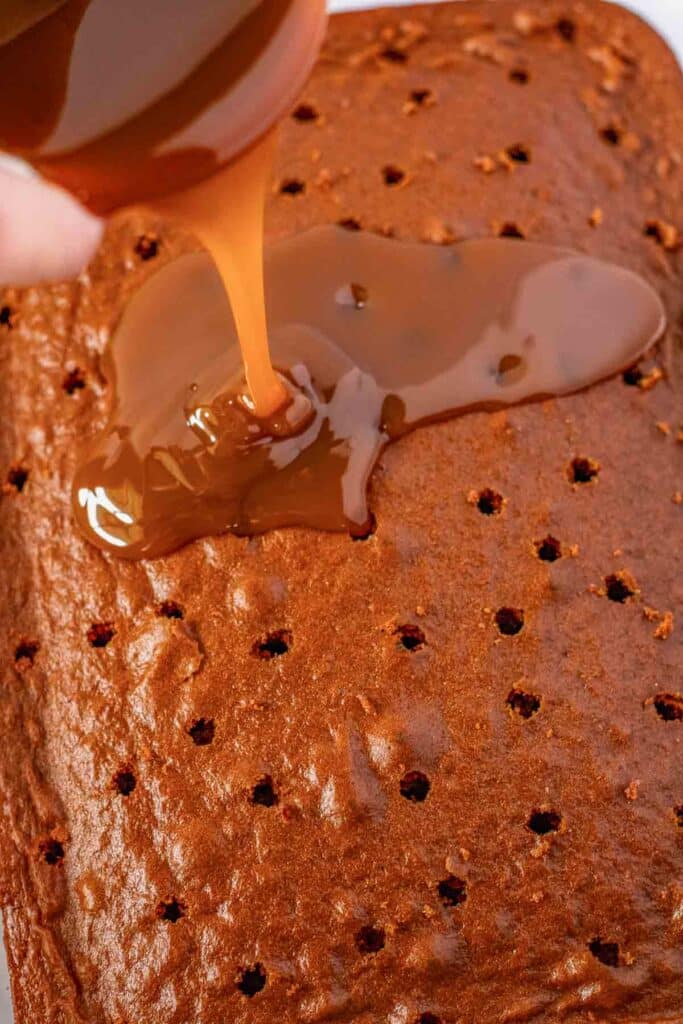 Caramel sauce being poured over a chocolate cake with holes poked in it.