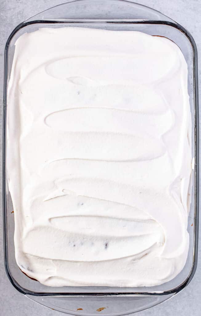 Chocolate caramel cake with cool whip spread evenly overtop in a large clear glass baking dish.