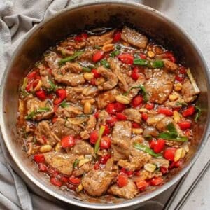 A skillet filled with cooked beef strips, red bell peppers, green onions, and peanuts in a rich brown sauce.