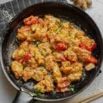 A black skillet containing a peanut butter chicken, red bell peppers, and green onions, garnished with sesame seeds.