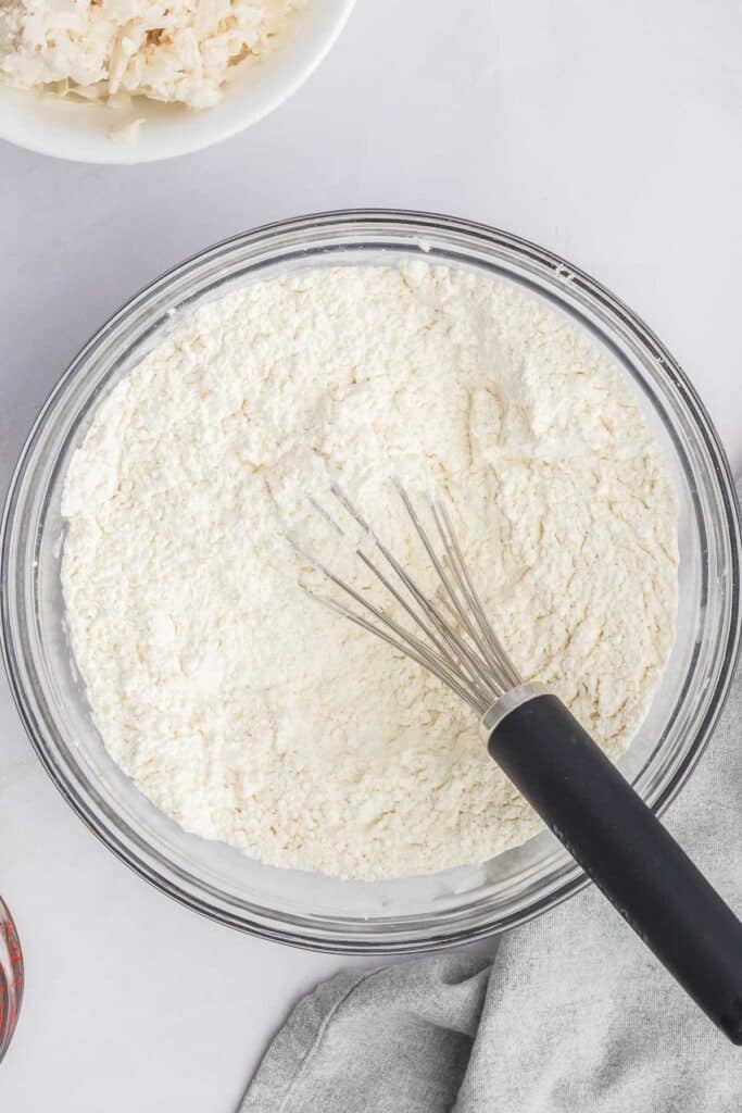 A glass bowl filled with flour mixture and a whisk.