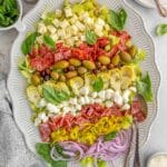 A platter of antipasto salad with two spoons on the side.