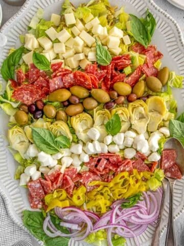 A platter of antipasto salad with two spoons on the side.