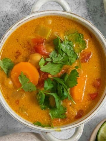 A white bowl of vibrant coconut curry soup garnished with cilantro.