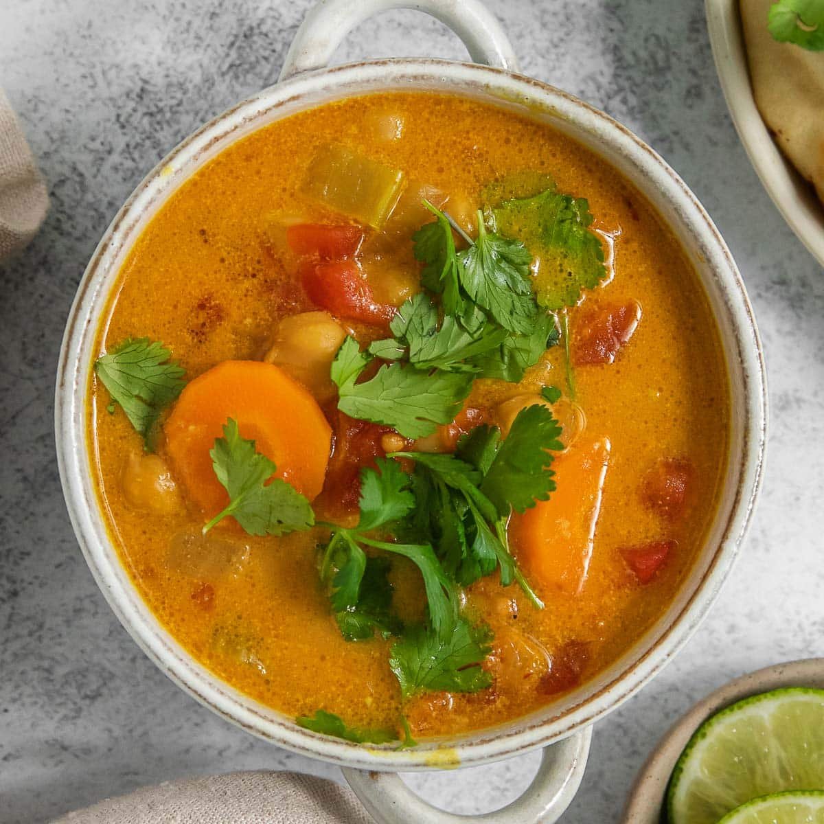 A white bowl of vibrant coconut curry soup garnished with cilantro.