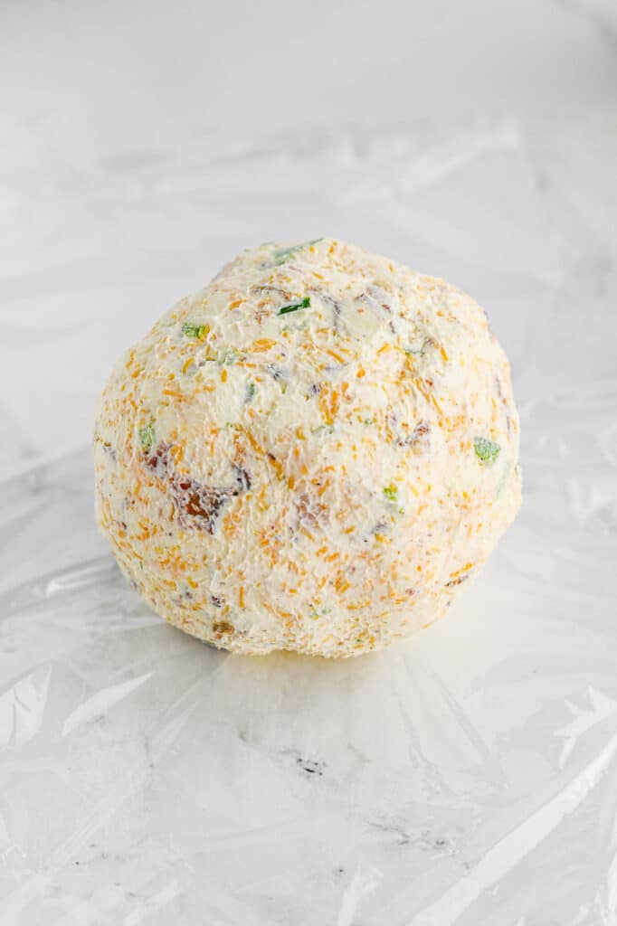 A round cheese ball with visible herbs and cheddar cheese on a white surface.