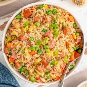 A white bowl of spam fried rice with a silver spoon on the side.