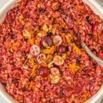A bowl of cranberry relish with chopped walnuts, orange zest, and whole cranberries, with a spoon in the bowl.