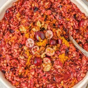 A bowl of cranberry relish with chopped walnuts, orange zest, and whole cranberries, with a spoon in the bowl.