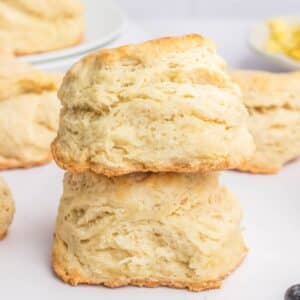 Two stacked, golden-brown homemade biscuits with flaky layers against a blurred background.