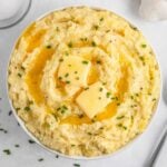 A bowl of creamy mashed potatoes topped with two pats of butter and sprinkled with chopped chives.