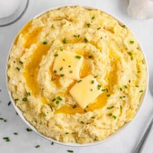 A bowl of creamy mashed potatoes topped with two pats of butter and sprinkled with chopped chives.