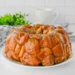 A glazed monkey bread on a white plate. A white mug and green plant are in the background.