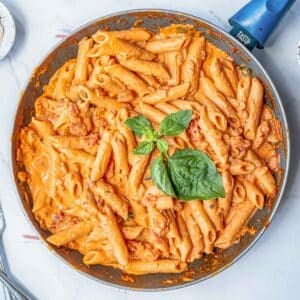 A pan of penne pasta tossed in a creamy italian pink sauce garnished with basil leaves.