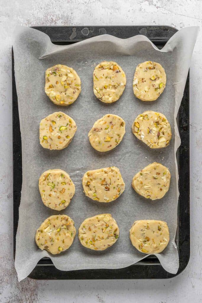 Unbaked pistachio shortbread cookies on a parchment-lined baking sheet.