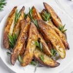 A white plate of rosemary roasted potatoes garnished with fresh rosemary sprigs on a marble surface.