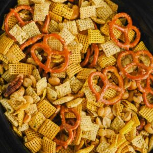 slow cooker filled with Chex mix recipe of pretzels, peanuts, and cereal squares.