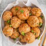 A bowl of thai chicken meatballs garnished with green onions and sesame seeds with chopsticks laying beside.