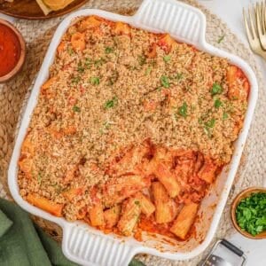 Chicken parmesan casserole topped with breadcrumbs is in a white casserole dish.