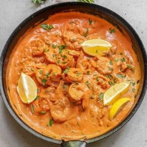 A pan of creamy garlic shrimp garnished with lemon wedges and chopped herbs.