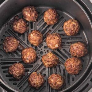 Meatballs cooking in an air fryer basket, evenly spaced and browned.