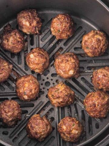 Meatballs cooking in an air fryer basket, evenly spaced and browned.