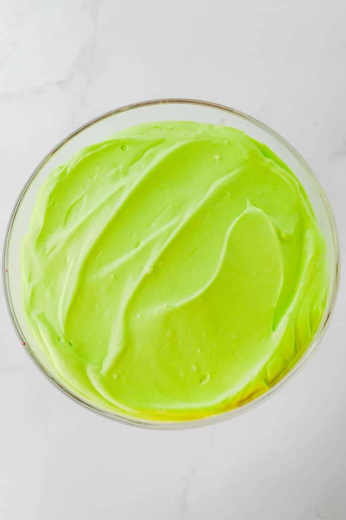 A trifle bowl of vibrant green pudding on a white marble background.