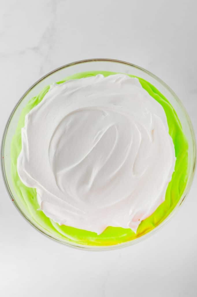 A trifle bowl of with green pudding topped with white whipped cream, viewed from above.