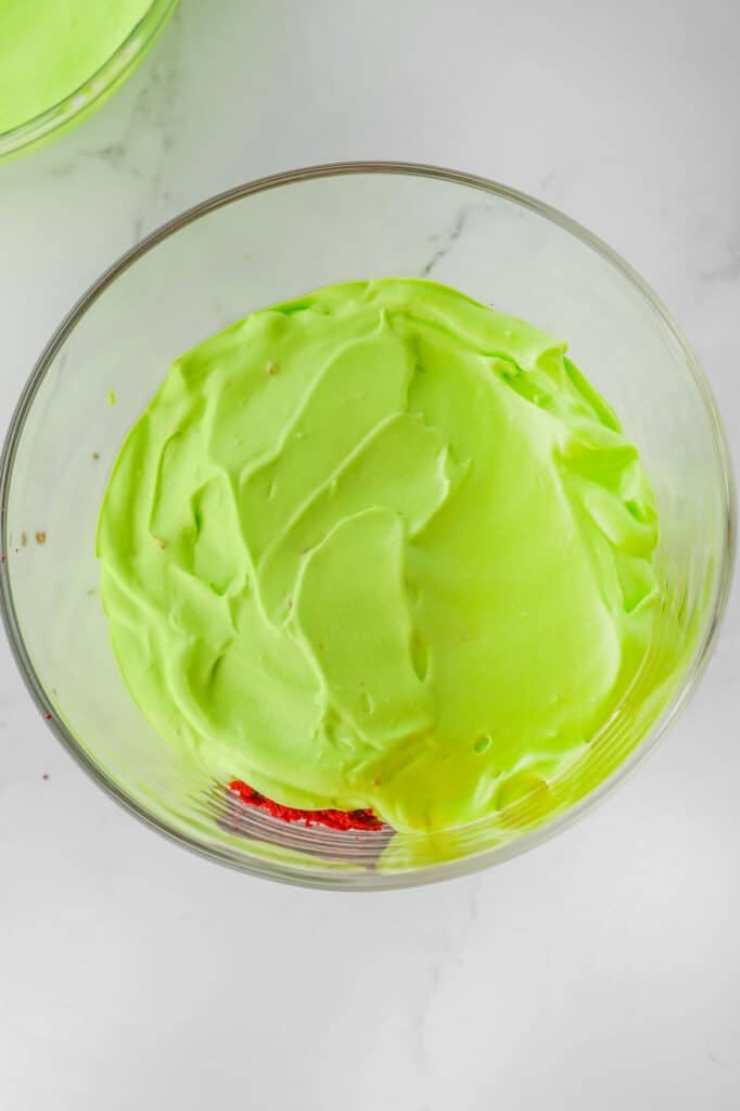 A clear glass bowl filled with vibrant green pudding placed on a white marble surface.
